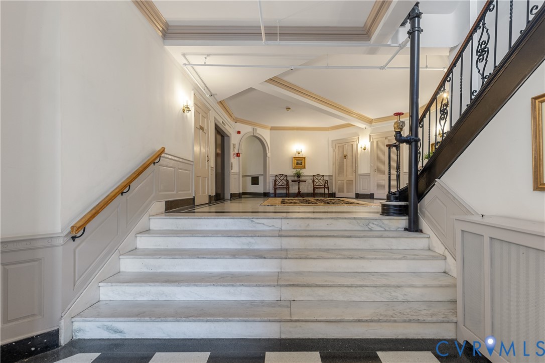 Foyer featuring stone stairs, a wrought-iron railing with a wood handrail, wainscoting, a vaulted ceiling, and checkerboard-pattern flooring