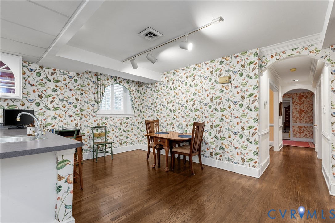 Wood-finish flooring, archway architectural detail, track lighting, and a kitchen peninsula with an integrated sink