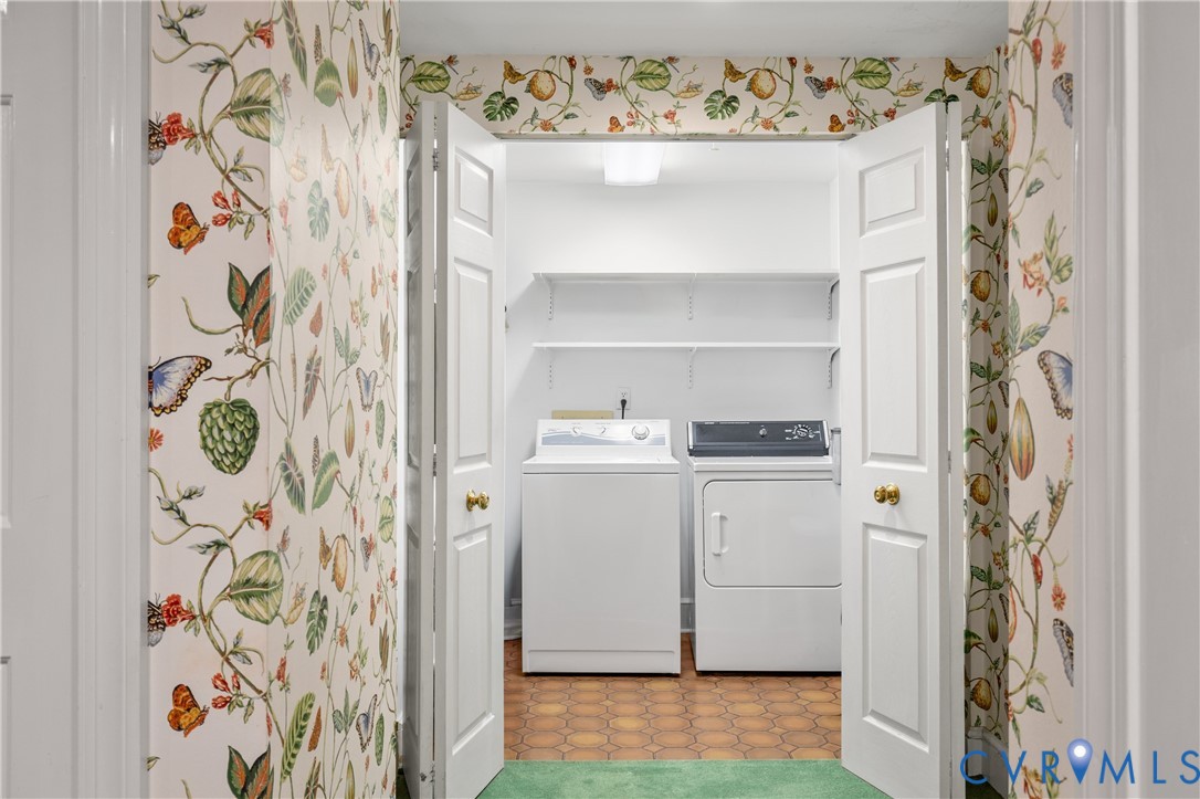 Laundry closet featuring dual white bi-fold doors, botanical print wallpaper, hexagonal tile flooring, and integrated wall-mounted shelving