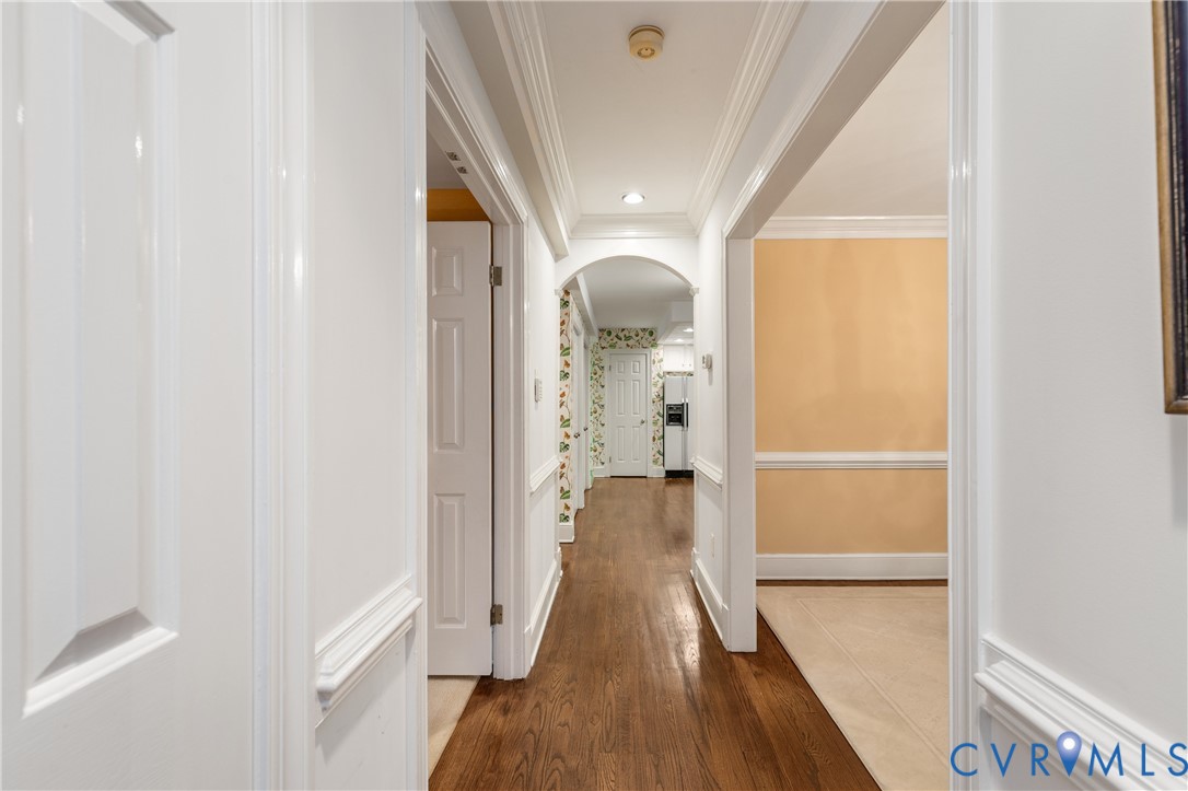 Hallway featuring wood-finish flooring, crown molding, chair rail trim, recessed lighting, and a decorative arched entryway