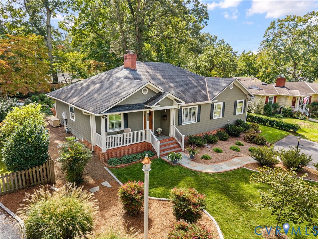 Siding exterior with contrasting shutters, covered front porch, brick steps, front yard with mature landscaping, and an extended driveway