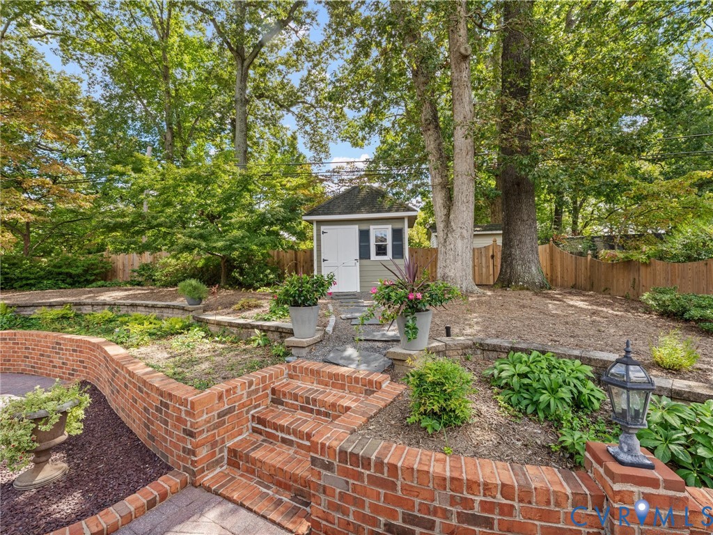 Terraced landscaping with brick retaining walls, integrated brick steps, a detached storage shed, and mature trees