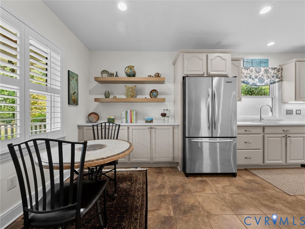 Stainless steel refrigerator, white shaker-style cabinetry, wood-finish flooring, white plantation shutters, and recessed lighting