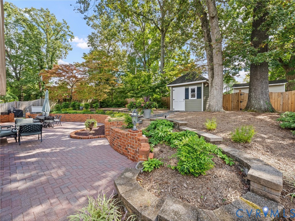 Expansive brick paver patio with a curved brick retaining wall, terraced landscaping beds, and a detached storage shed