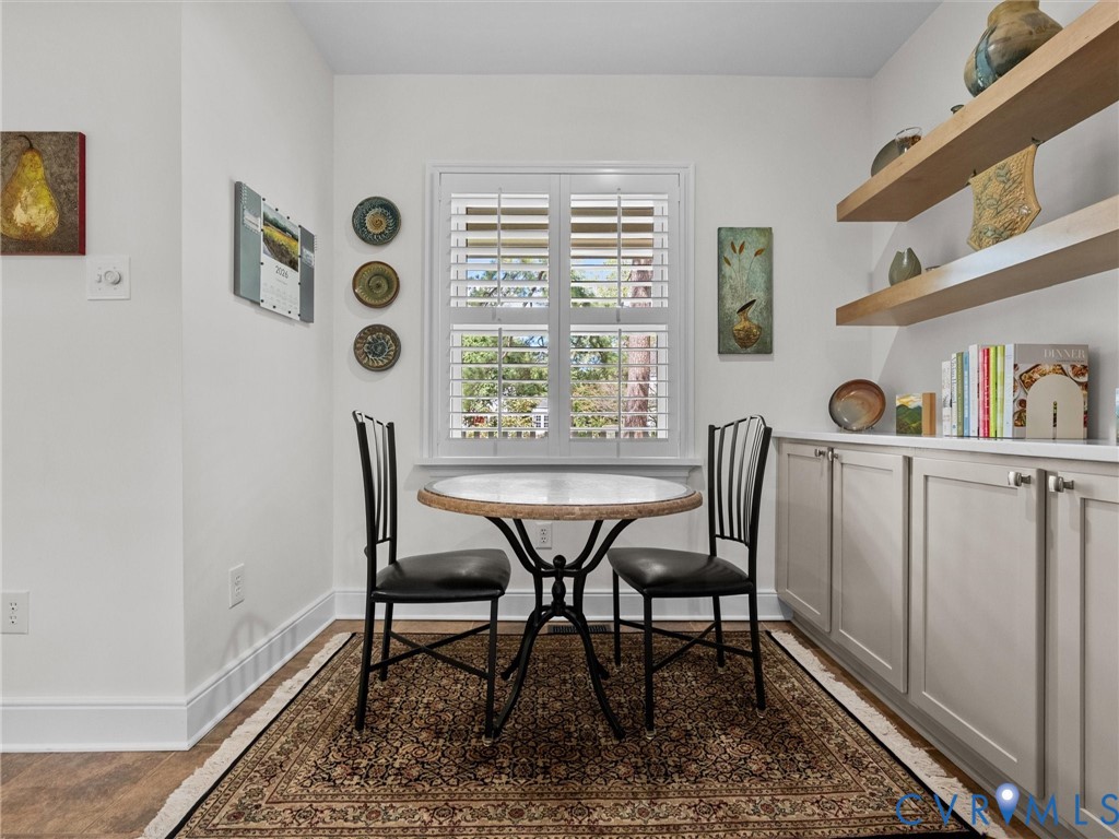 White plantation shutters, built-in lower cabinetry with silver hardware, upper wood-finish shelving, wood-finish flooring, and white wall finishes