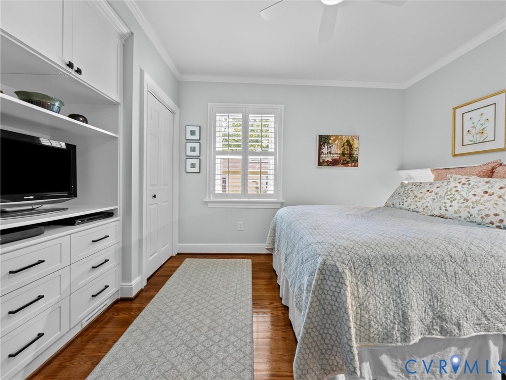 Built-in cabinetry with shelving and drawers, wood-finish flooring, plantation shutters, crown molding, and a ceiling fan
