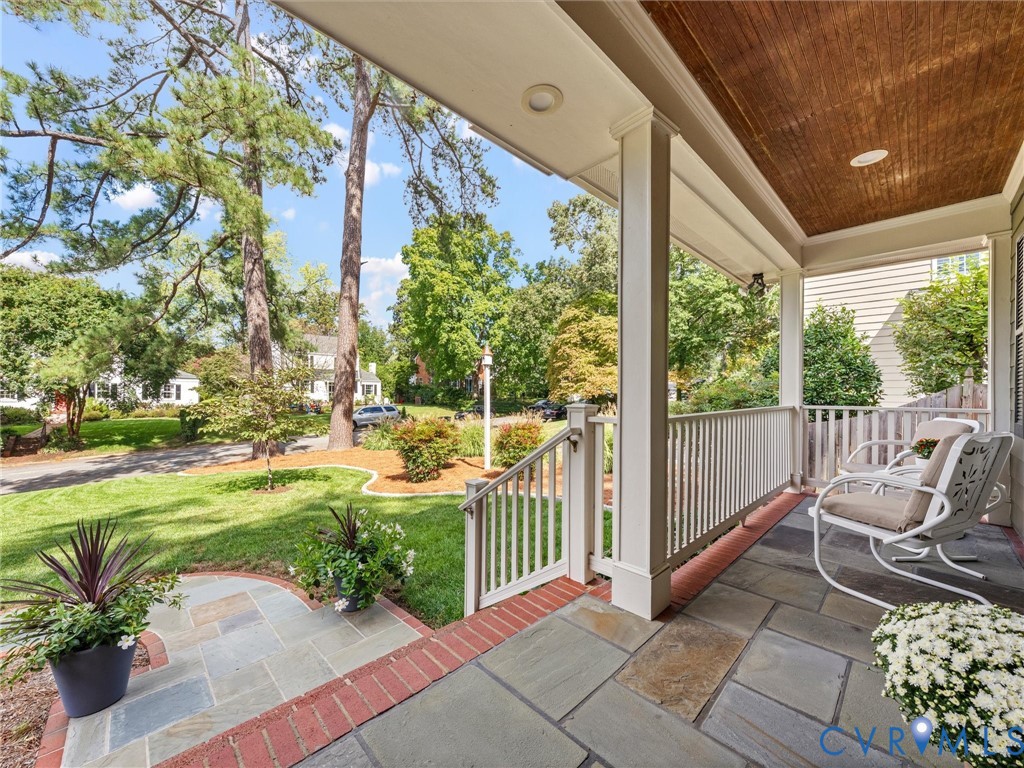 Covered front porch featuring flagstone flooring, white railing, and a wood-paneled ceiling