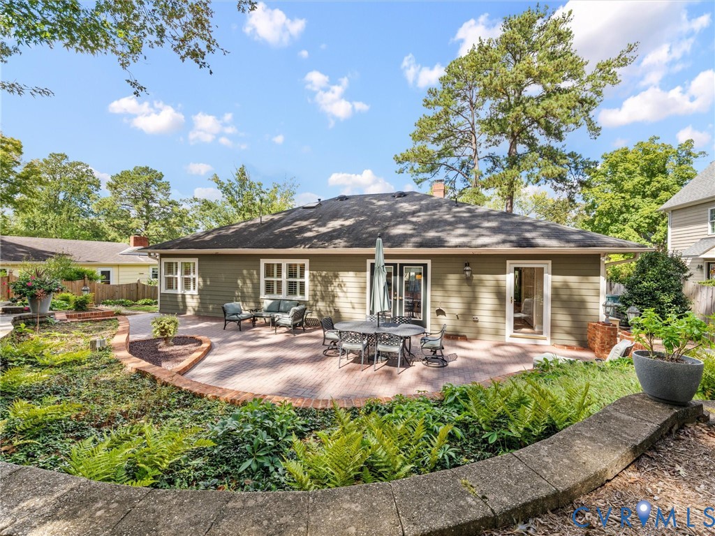 Expansive brick paver patio with a low stone retaining wall, featuring exterior siding, multiple windows, and two glass entry doors