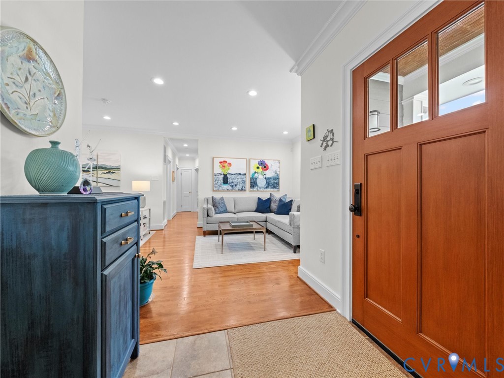 Paneled wood entry door with clear glass lites and dark hardware, light tile flooring, wood-finish flooring, recessed lighting, and white crown molding