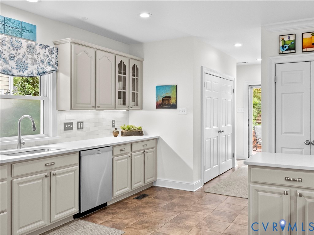 Kitchen featuring light-toned cabinetry, white countertops, subway tile backsplash, and a stainless steel dishwasher