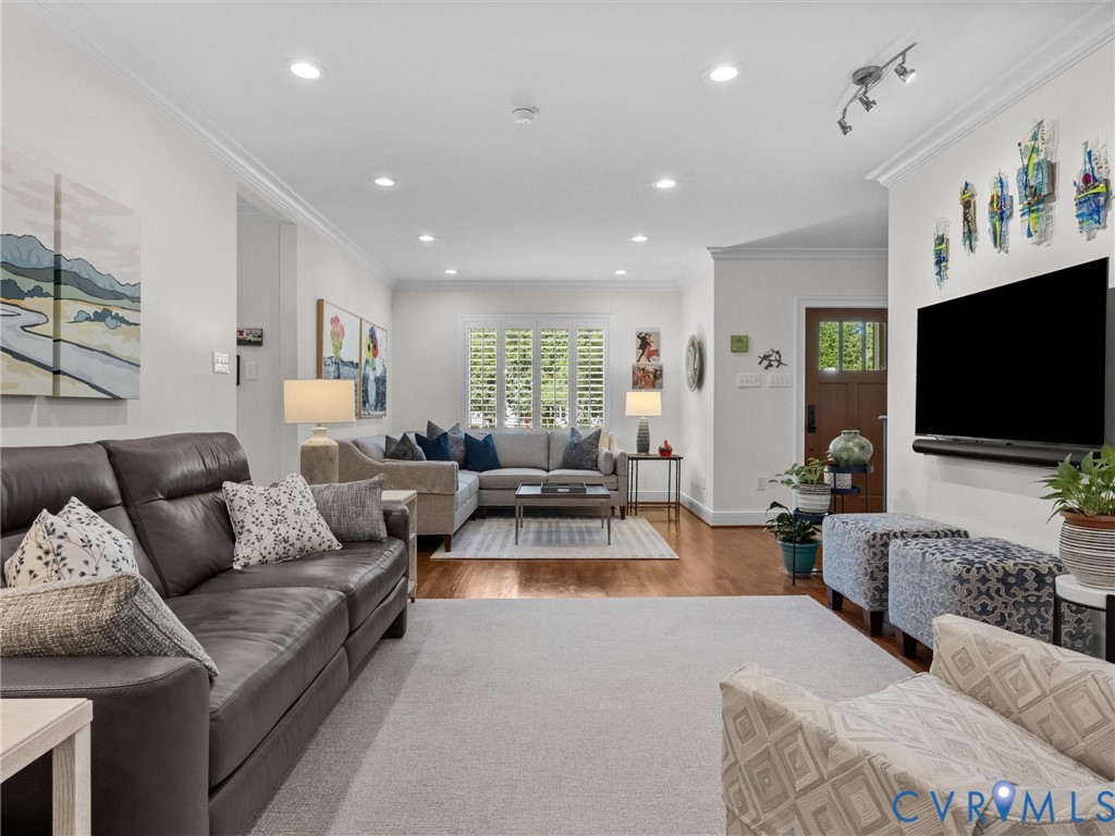 Recessed lighting, wood-finish flooring, white plantation shutters, crown molding, and a solid wood entry door with glass paneling