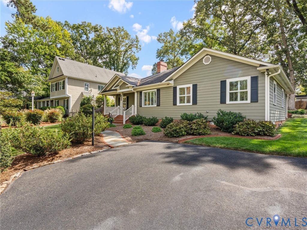 Siding exterior with black shutters, mature landscaping, paved driveway, and covered entry porch with white railings