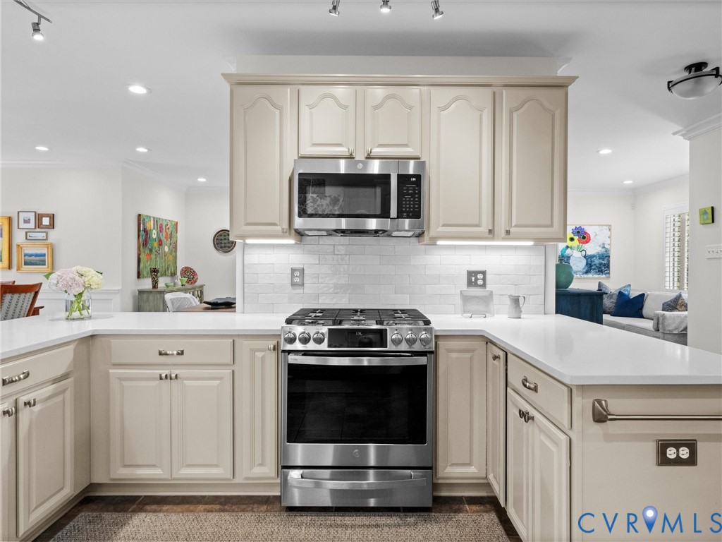Kitchen featuring stainless steel range, built-in microwave, white subway tile backsplash, light-toned cabinetry, and white countertops