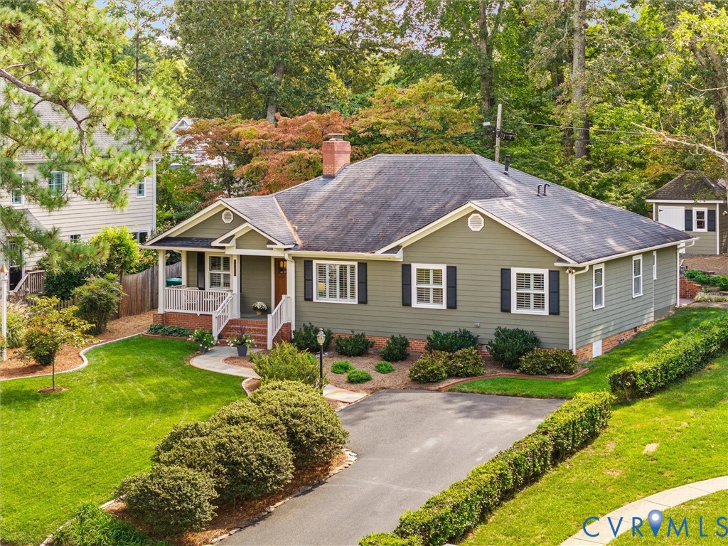 Expansive lawn with mature trees, paved driveway, covered front porch, and a detached outbuilding