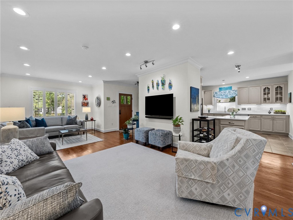 Recessed lighting, wood-finish flooring, white plantation shutters, built-in kitchen cabinetry, and a kitchen island with seating