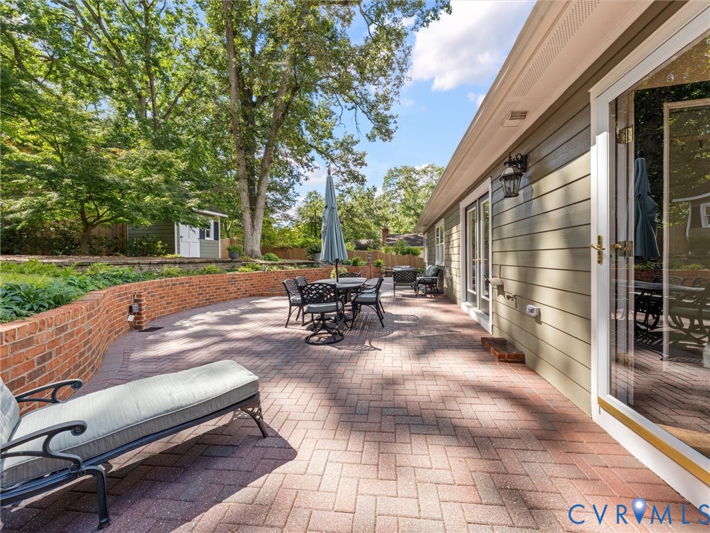 Expansive brick paver patio featuring a curved brick retaining wall, exterior lighting fixtures, and multiple glass-paneled doors