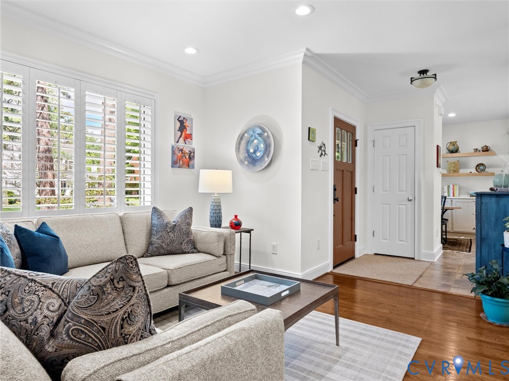 White plantation shutters, recessed lighting, crown molding, wood-finish flooring, and a paneled entry door