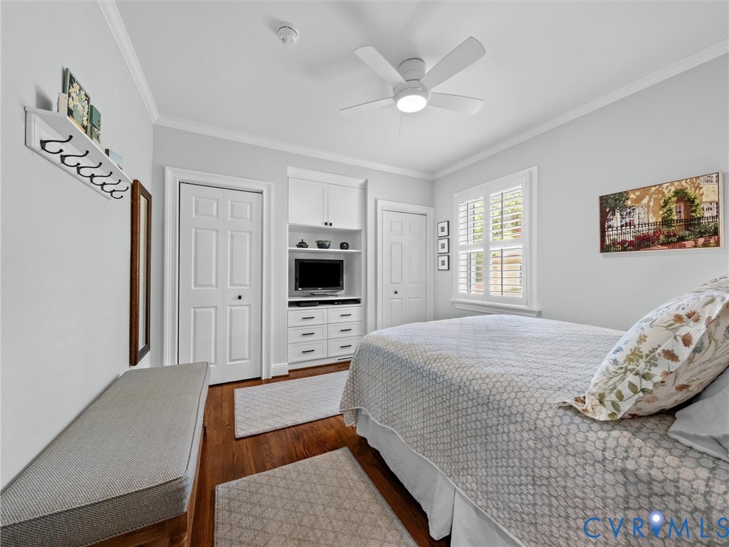 Wood-finish flooring, plantation shutters, crown molding, built-in cabinetry with drawers, and a ceiling fan with integrated lighting