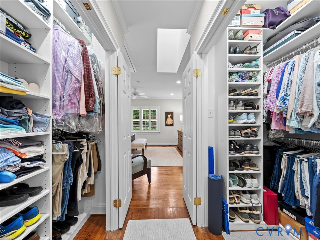 Custom closet system with white shelving, multiple hanging rods, dedicated shoe storage, and wood-finish flooring