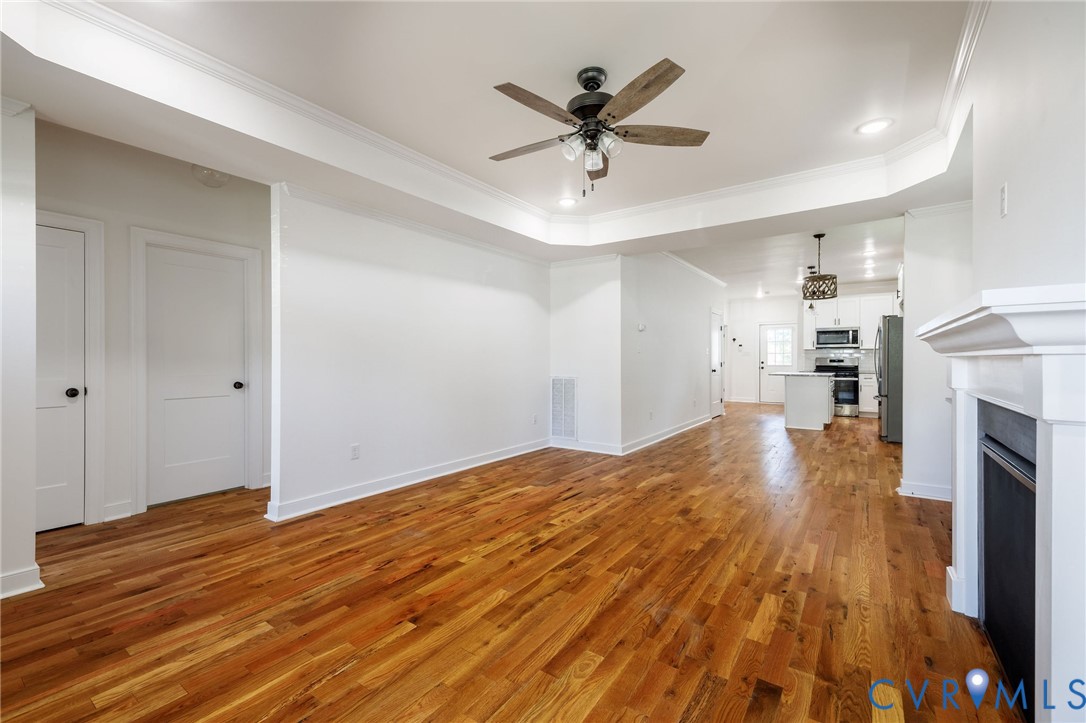 Living area featuring wood-finish flooring, recessed lighting, crown molding, tray ceiling, and a fireplace with a white mantle