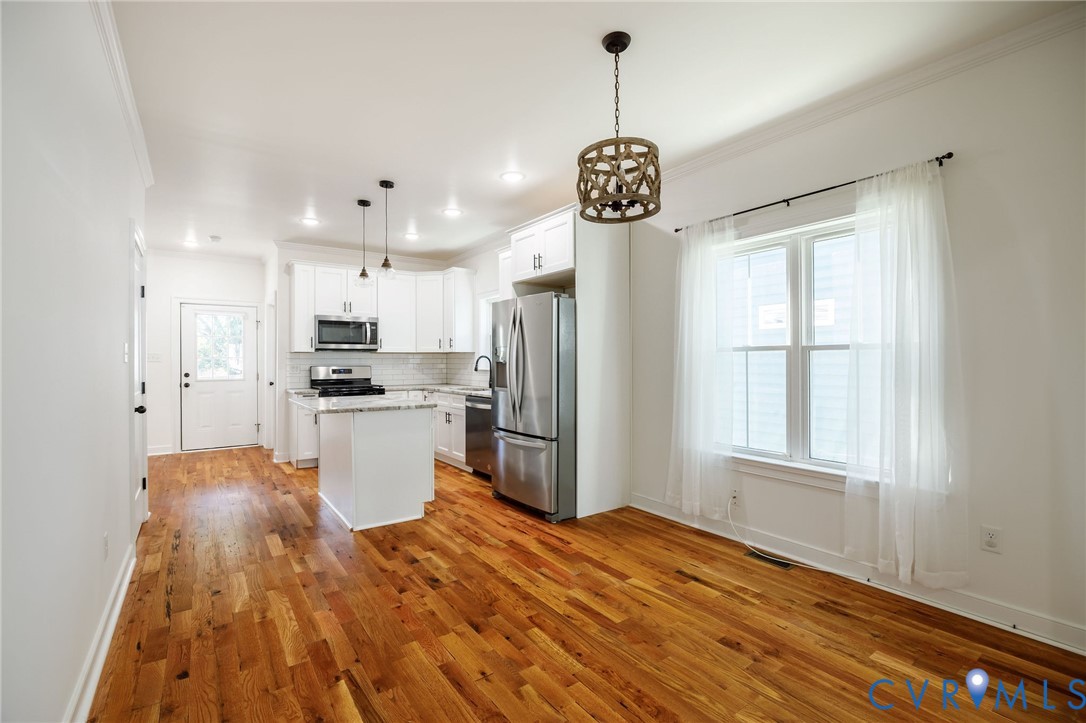 Kitchen featuring wood-finish flooring, white cabinetry, a center island with stone-finish countertops, stainless steel appliances, and decorative pendant lighting