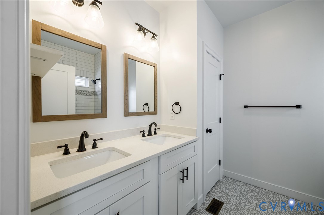 Double vanity featuring white cabinetry, stone-composite countertops, rectangular under-mount sinks, matte black fixtures, and framed wood-finish mirrors