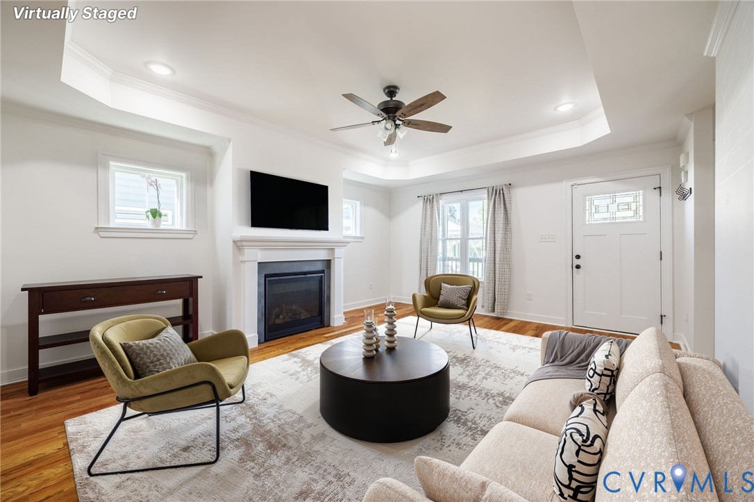 Tray ceiling with recessed lighting, fireplace with a classic mantel, wood-finish flooring, and exterior door with decorative glass panel
