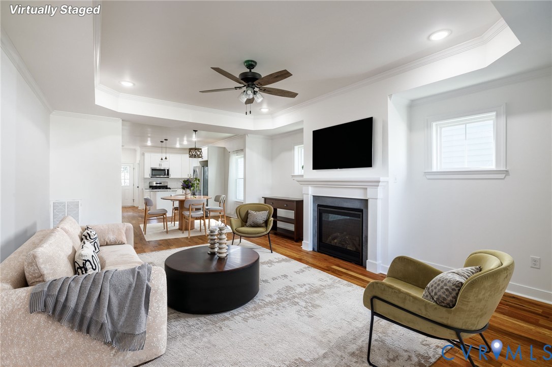 Tray ceiling featuring recessed lighting and a ceiling fan, fireplace with a mantel, and wood-finish flooring