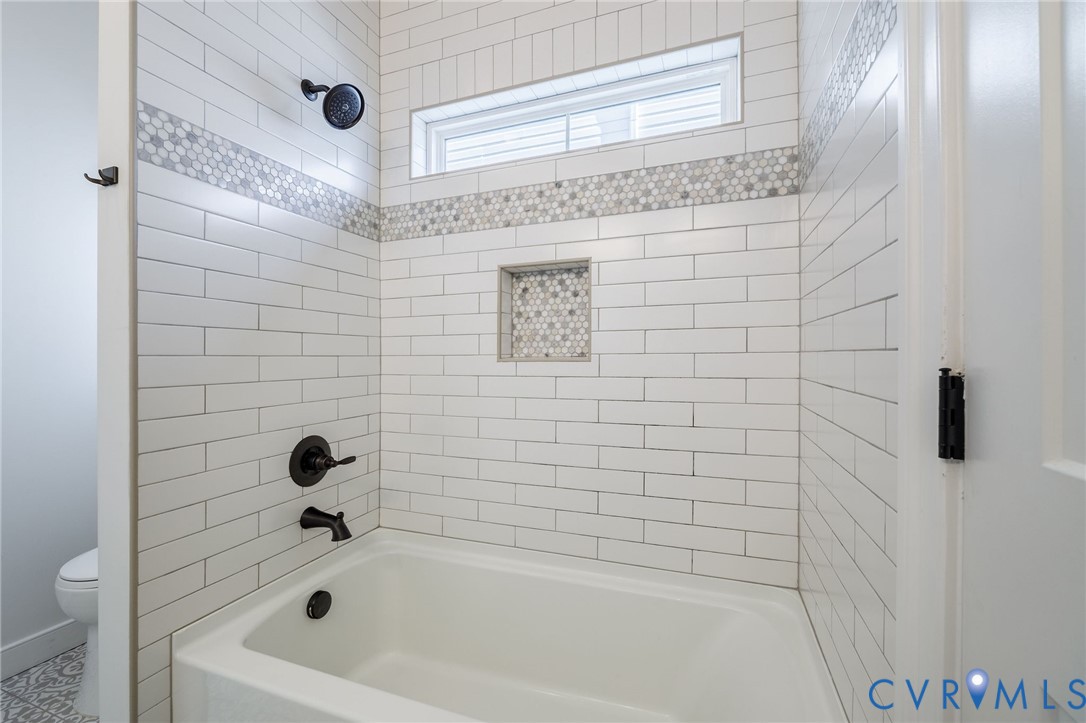 White subway tile surround with decorative hexagonal mosaic accent tile, matte black shower fixtures, built-in tiled niche, and transom window