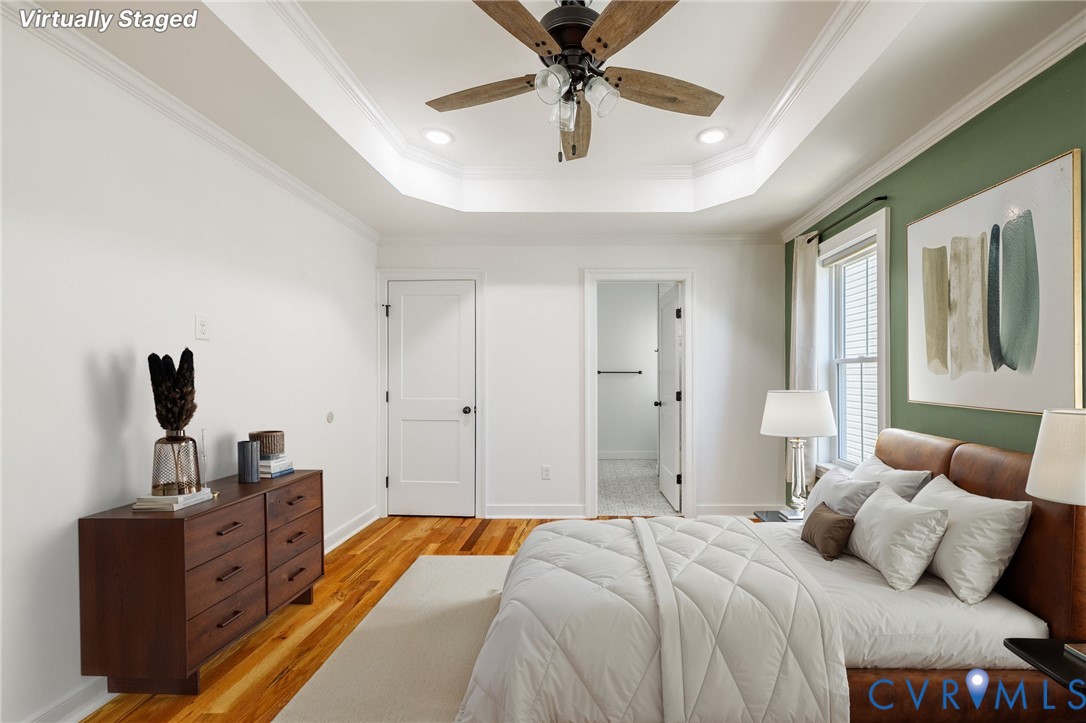 Tray ceiling featuring a central multi-blade ceiling fan, wood-finish flooring, and crown molding