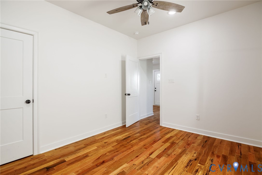 Interior space featuring wood-finish flooring, white walls, two-panel interior doors with black hardware, and a ceiling fan with integrated lighting