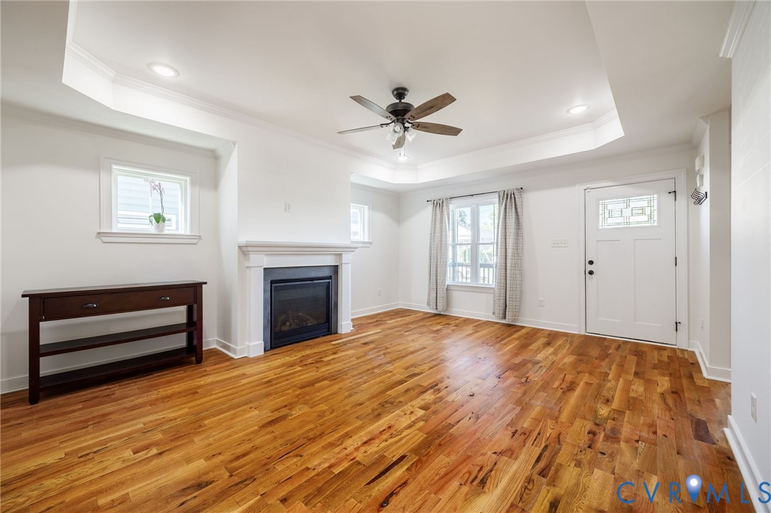 Tray ceiling, wood-finish flooring, recessed lighting, fireplace with a decorative mantel, and an exterior entry door with glass paneling