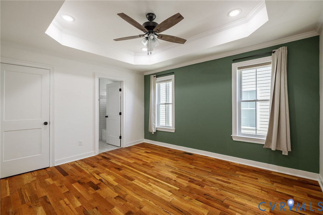Tray ceiling featuring a central ceiling fan with integrated lighting, wood-finish flooring, and two double-hung windows