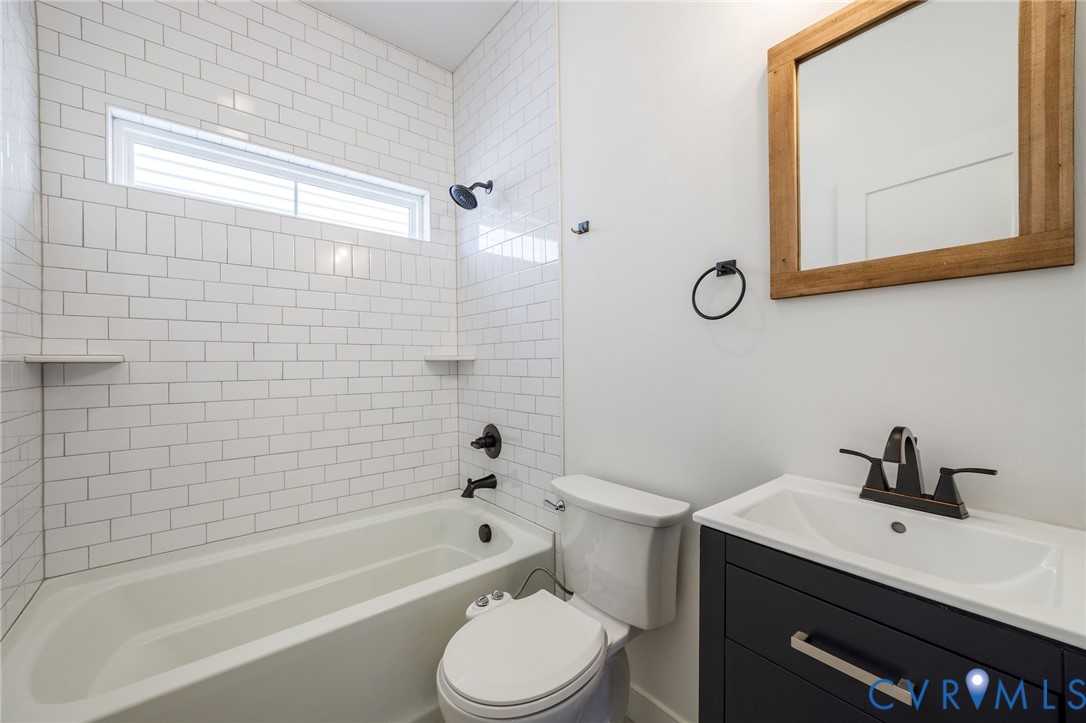 Bathroom featuring white subway tile tub surround, dark-finish hardware, built-in shelving, a deep-toned vanity with a white basin, and a wooden-framed wall mirror