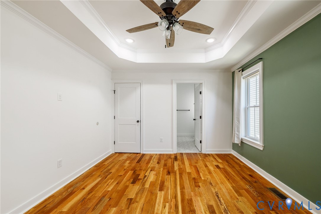 Tray ceiling featuring crown molding, wood-finish flooring, multi-pane window with trim, and ceiling fan with integrated lighting