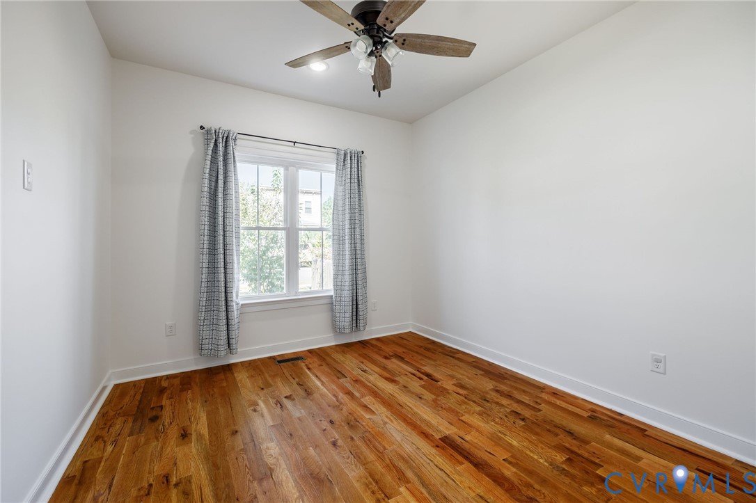 Wood-finish flooring, neutral walls, and a ceiling fan with integrated lighting
