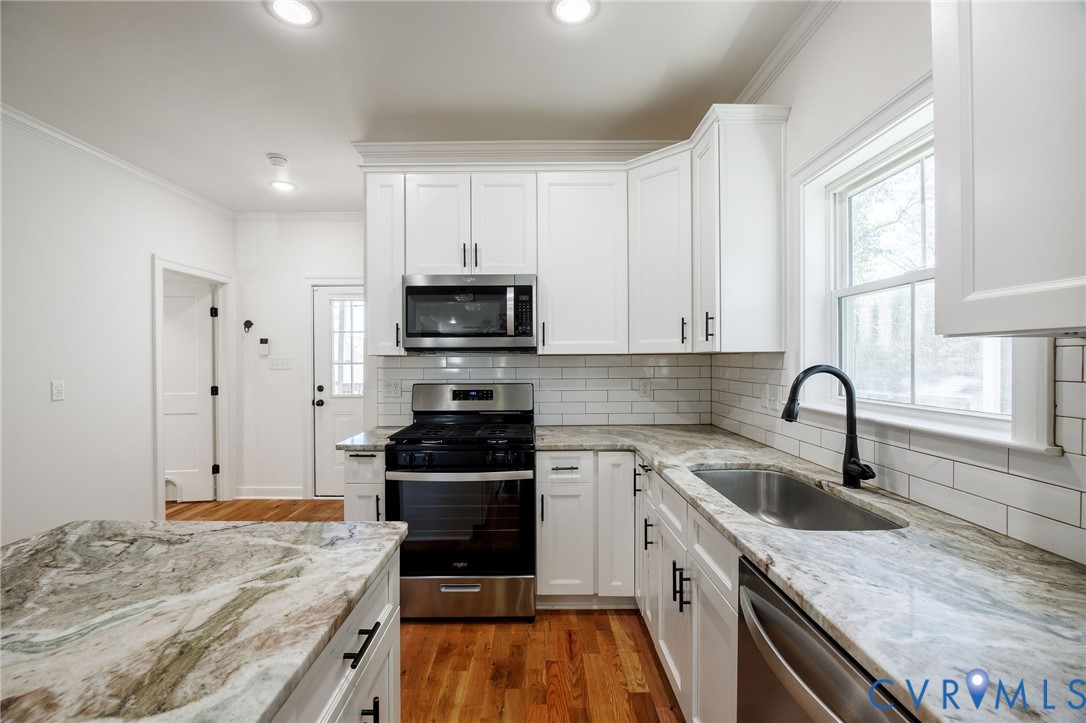 Kitchen featuring white shaker-style cabinetry, stone-patterned countertops, subway tile backsplash, stainless steel appliances, and wood-finish flooring