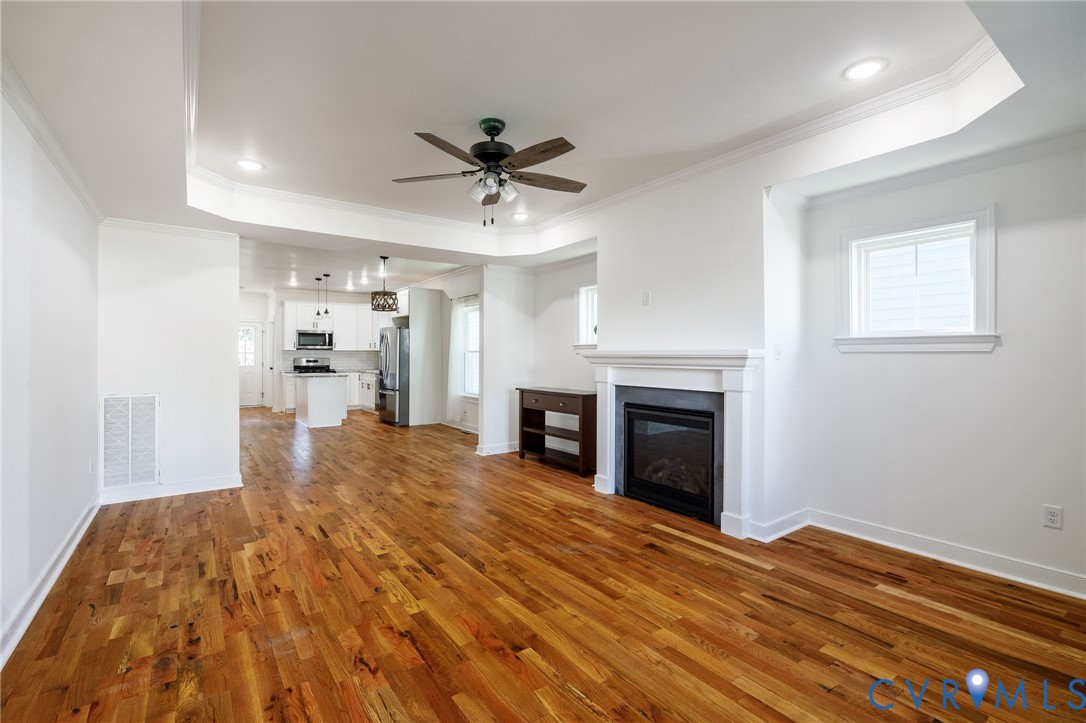 Open concept interior featuring wood-finish flooring, recessed lighting, a tray ceiling, and a fireplace with a white mantel