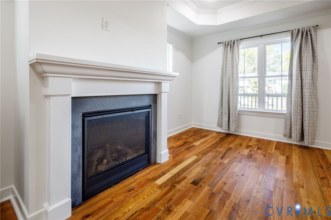 Gas fireplace with a stone-surround and classic white mantel, wood-finish flooring, and tray ceiling