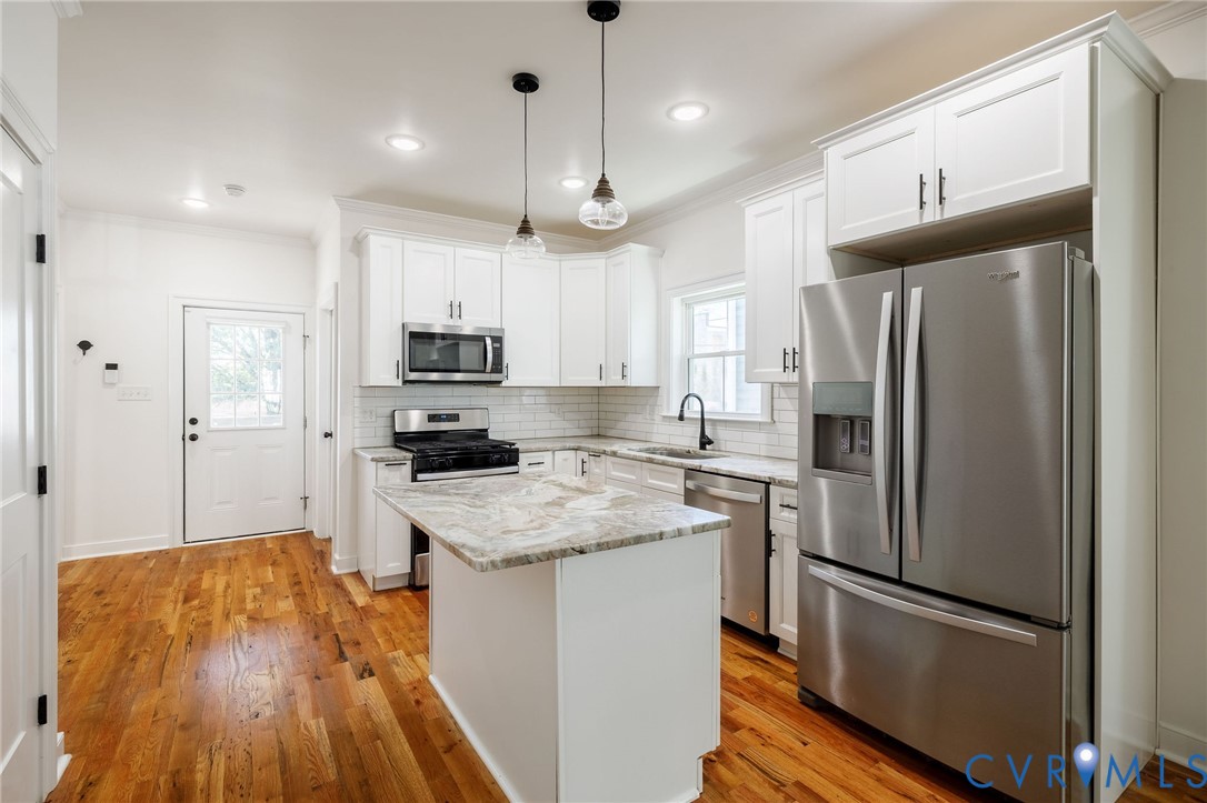 Kitchen featuring white shaker-style cabinetry, stone-finish countertops, stainless steel appliances, a center island, and wood-finish flooring