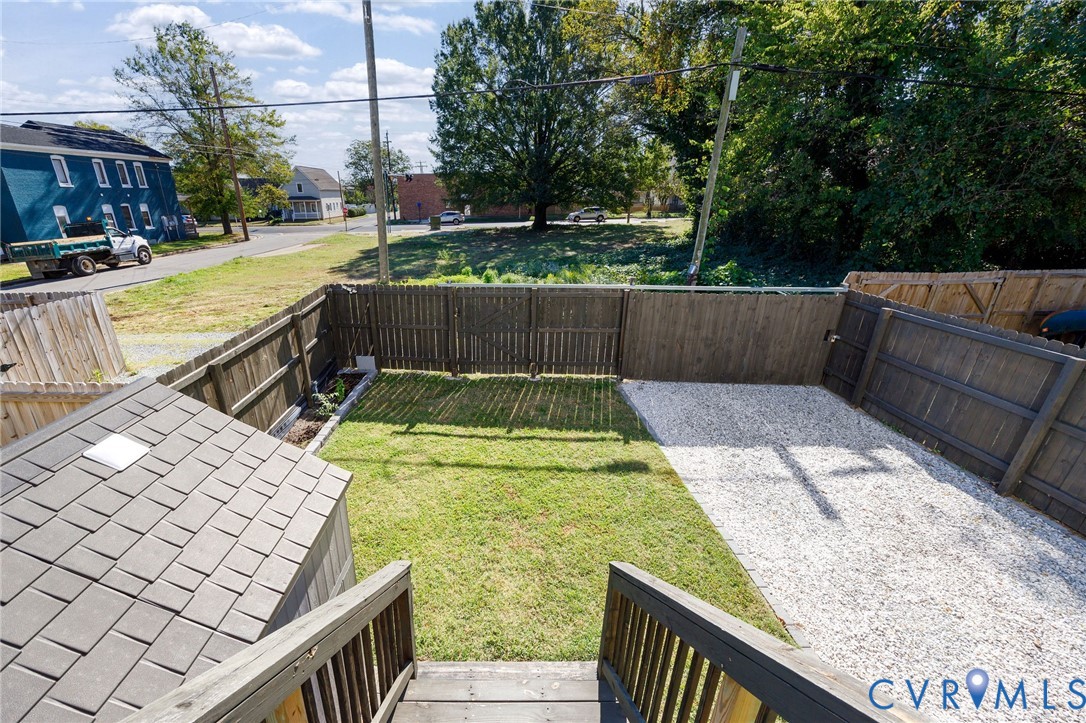 Enclosed backyard featuring wood fencing, a grass lawn, gravel surfacing, and a shingle-roofed exterior structure