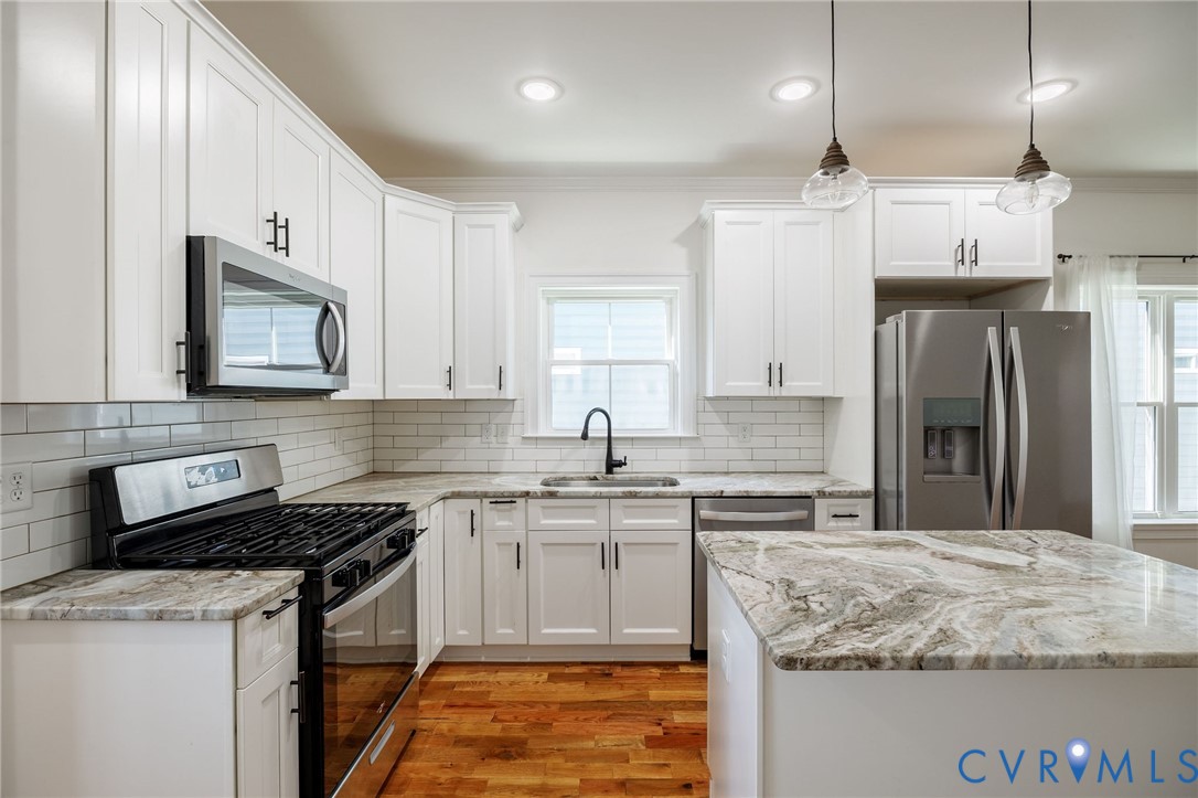 Kitchen featuring white shaker-style cabinetry, natural stone countertops, a subway tile backsplash, stainless steel appliances, and wood-finish flooring