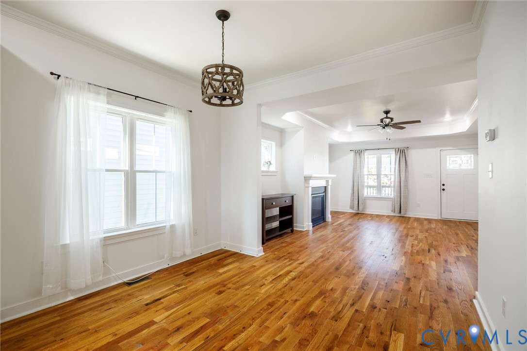Hardwood flooring, crown molding, decorative drum pendant lighting, fireplace with mantel, and recessed tray ceiling