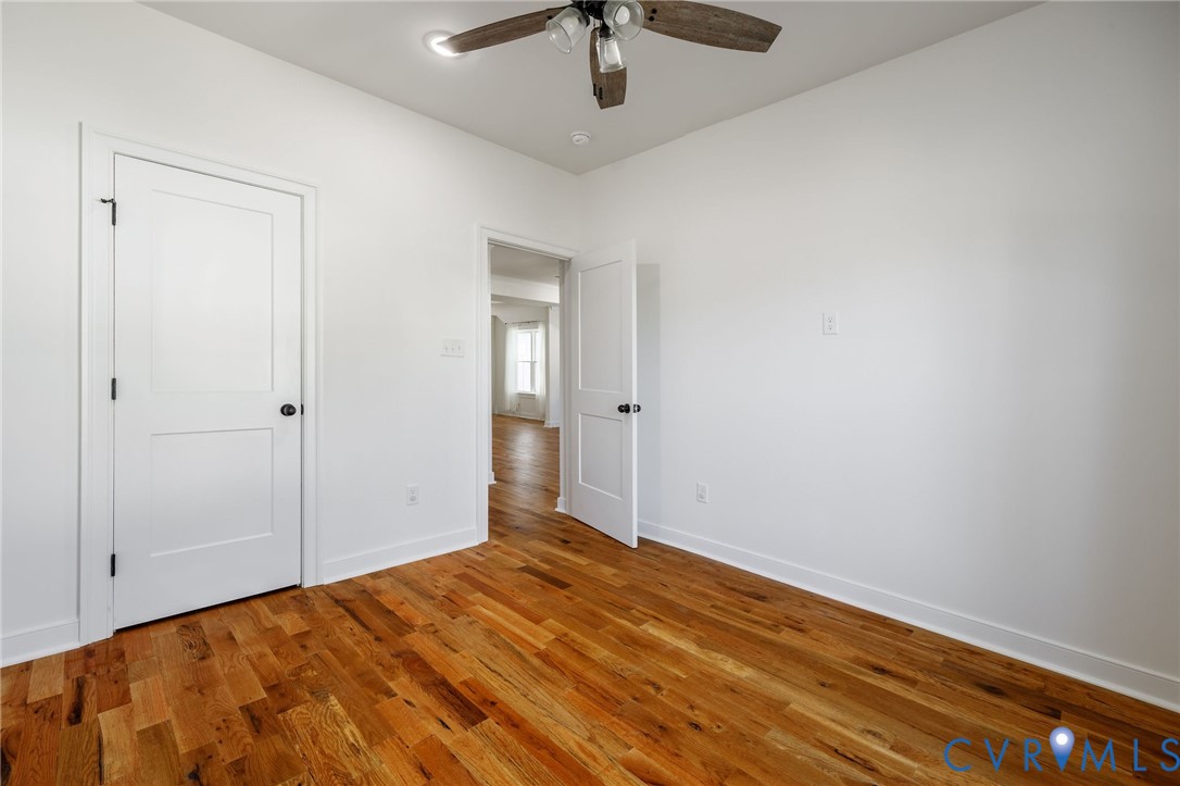 Room featuring wood-finish flooring, two-panel shaker-style interior doors with matte black hardware, and a ceiling-mounted light fixture with a fan