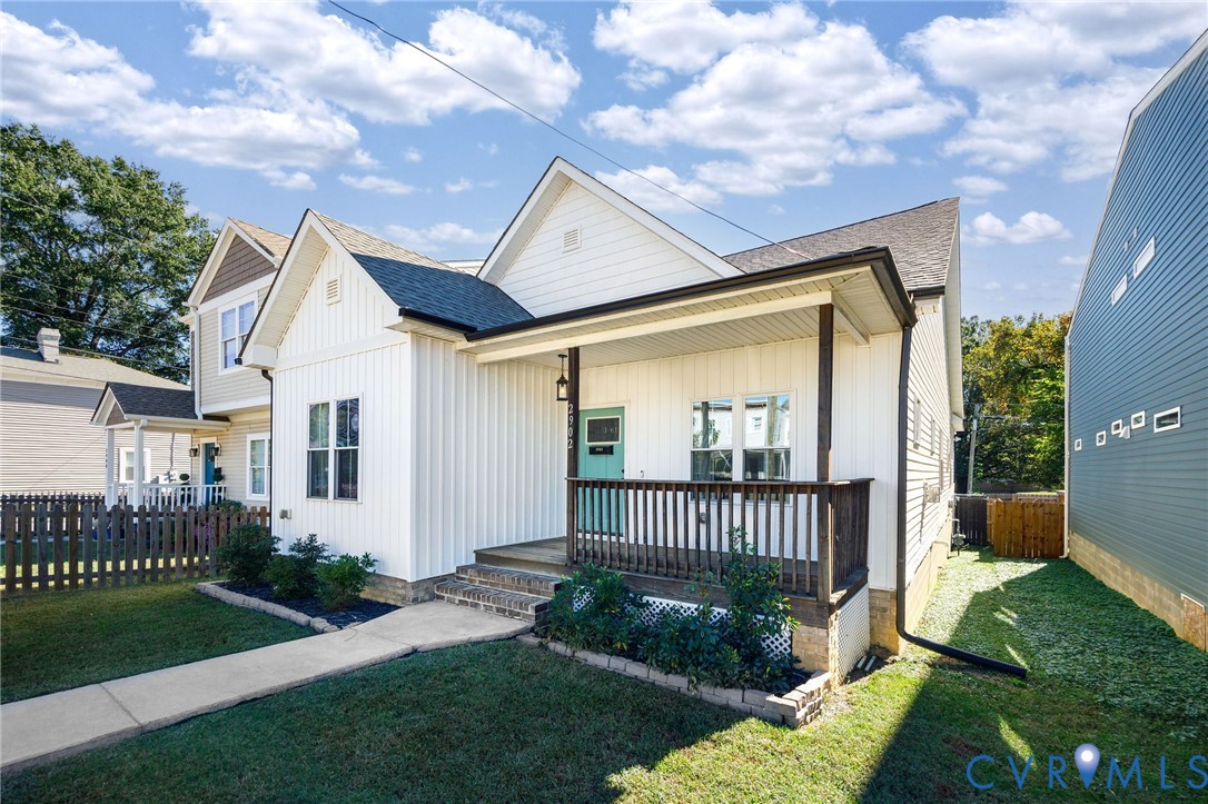 Vertical board-and-batten siding exterior featuring a covered front porch, dark-stained wooden railings, and a concrete walkway