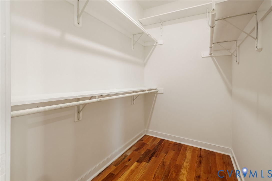 Walk-in storage space featuring wood-finish flooring and tiered metal shelving units with integrated clothing rods