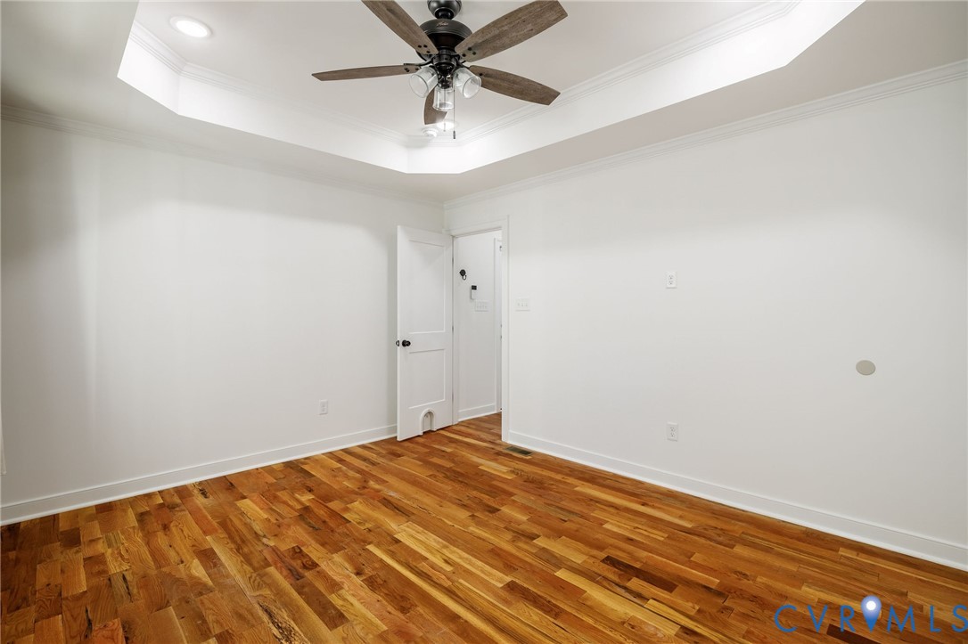 Tray ceiling featuring recessed lighting and a central multi-blade ceiling fan with integrated lighting, complemented by wood-finish flooring and solid-core interior doors