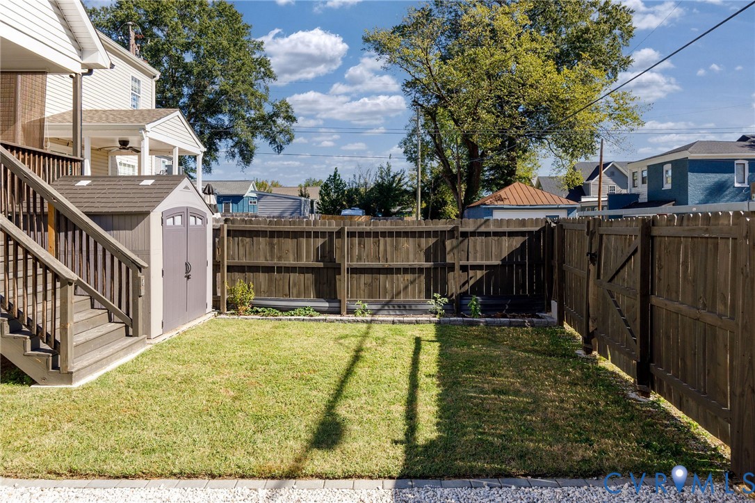 Fenced backyard featuring a manicured lawn, raised stone-bordered garden bed, and a resin storage shed