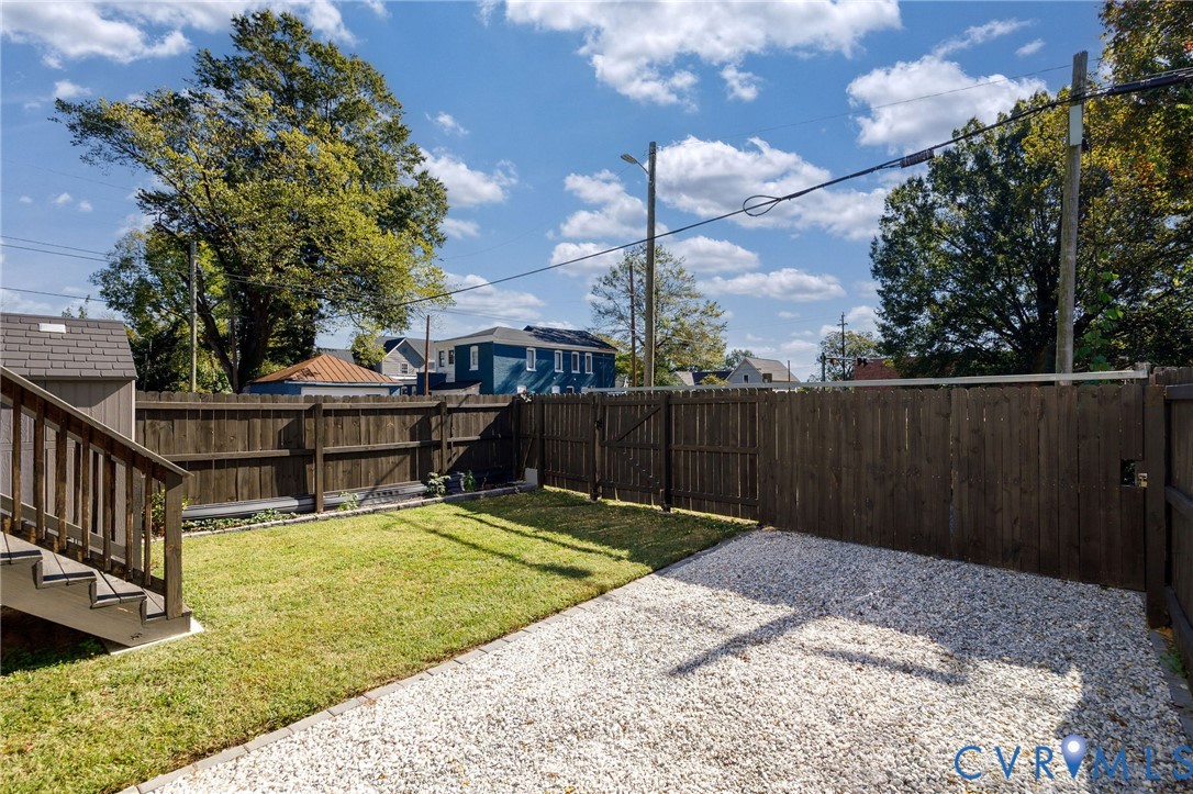 Backyard featuring a grass lawn, gravel patio area, wooden privacy fencing, and exterior staircase