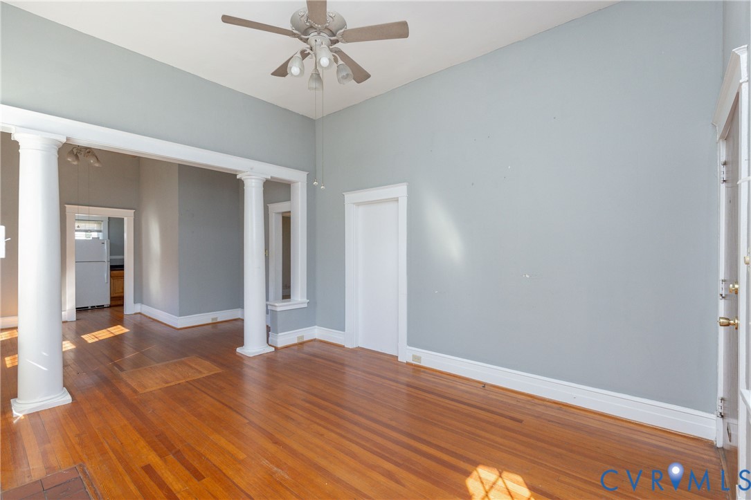 High ceilings, wood-finish flooring, white structural columns, and a multi-light ceiling fan fixture